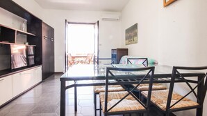 A dining area with a glass table and wicker chairs, a kitchen with dark cabinets, and a view through an open door to an outdoor patio.