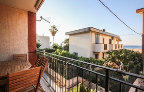 A balcony with wooden furniture, a view of a building with a balcony, and a palm tree.