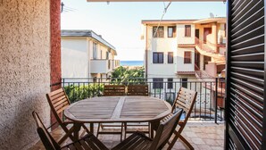 A balcony with a wooden table and chairs, overlooking a residential area with buildings and a view of the sea.