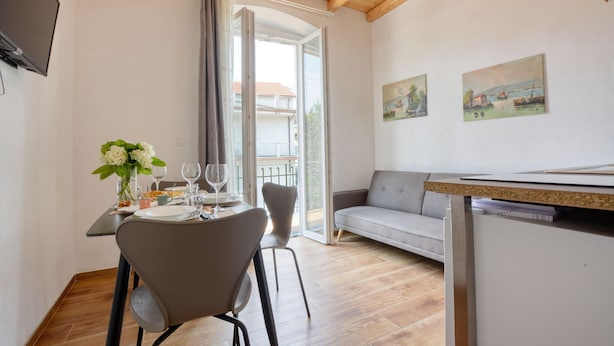 Un coin repas avec une table dressée pour deux personnes, un canapé gris et un téléviseur fixé au mur.
