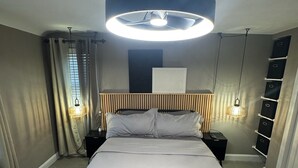 A modern bedroom with a large bed, two bedside tables, a headboard, a ceiling light, and a built-in shelving unit. - Charming 2-bedroom, 2-bathroom house in peaceful Mount Rainier. (Mount Rainier)