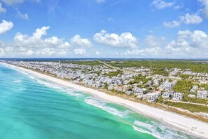 Un área residencial costera con propiedades frente a la playa, cielo despejado y una vista distante del horizonte.
