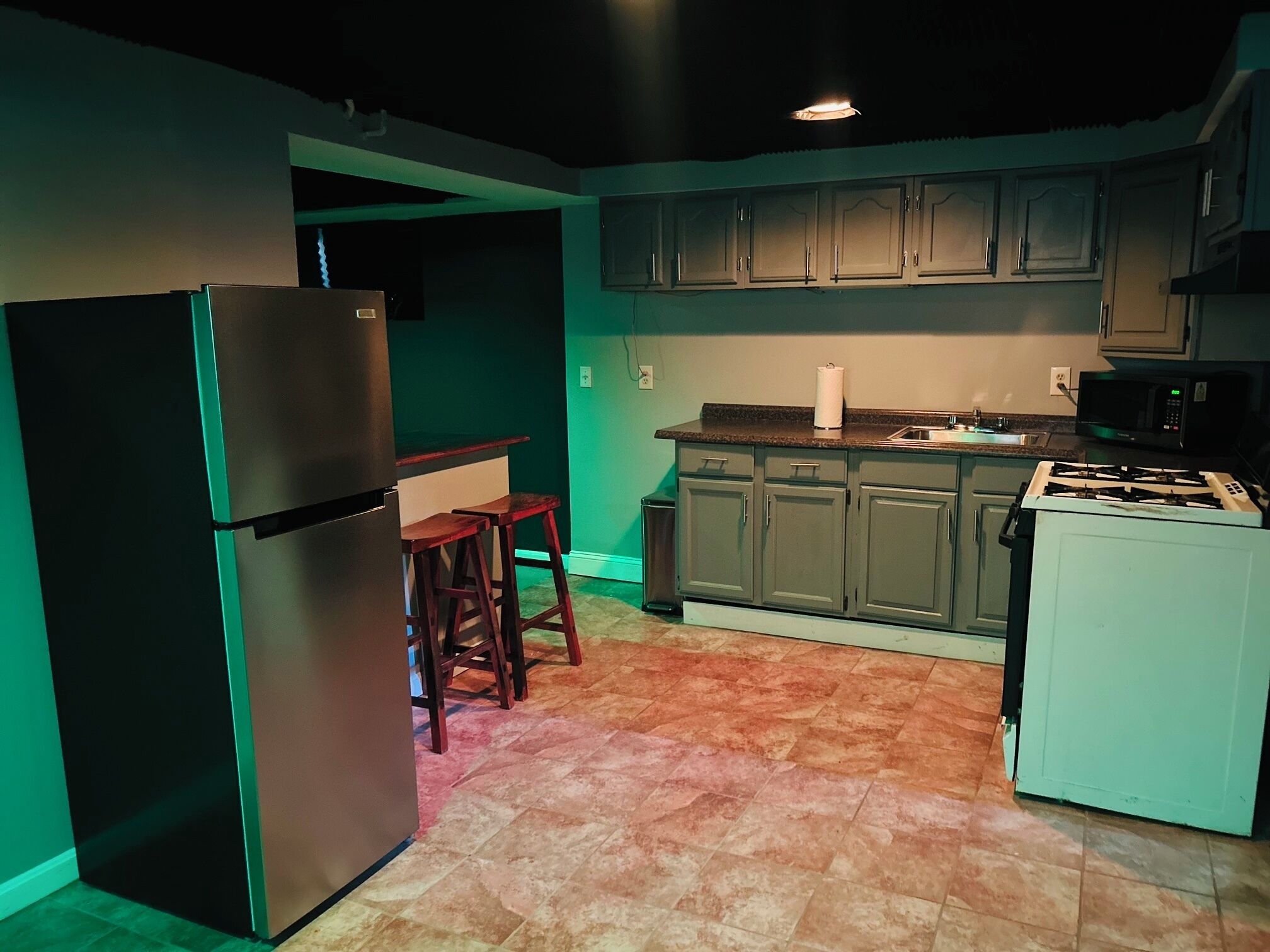A compact kitchen with a refrigerator, stove, and wooden stools.