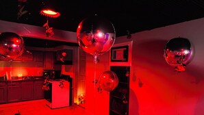 Une pièce éclairée d’une lumière rouge d’ambiance, avec un coin cuisine et plusieurs boules à facettes.