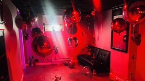 Une pièce avec un canapé en cuir noir, des ballons rouges et des miroirs aux murs.