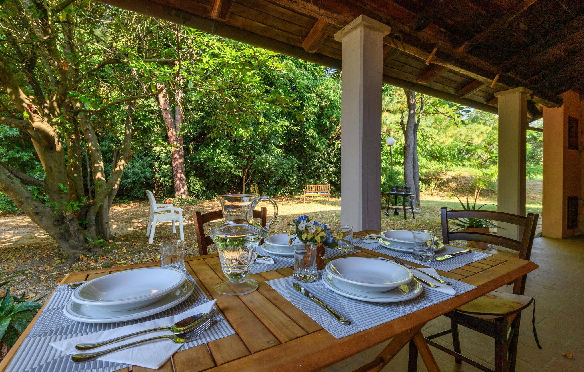 Un espace de restauration en plein air avec une table en bois prévue pour quatre personnes, entouré d’une végétation luxuriante et abrité par une structure couverte.