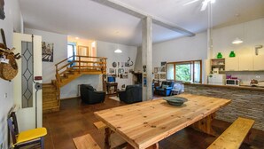 Un amplio salón con una mesa de comedor de madera, una escalera y una zona de cocina.