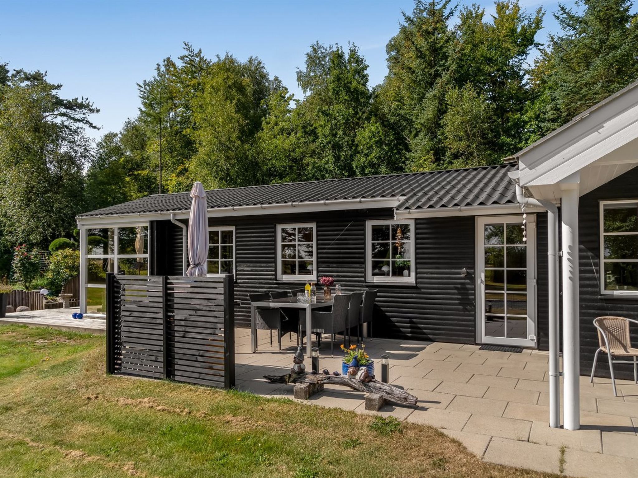 Et sort træhus med terrasse, overdækket siddeområde og have.