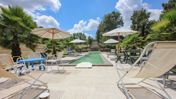 A pool area with lounge chairs, umbrellas, and a stone wall in the background. - Gorgeous home in Roma (Roma)