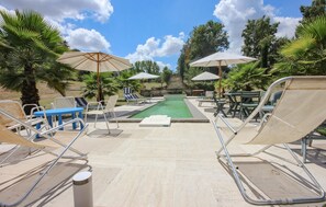 Un espace piscine aménagé avec des chaises longues, des parasols et un mur de pierre en arrière-plan.