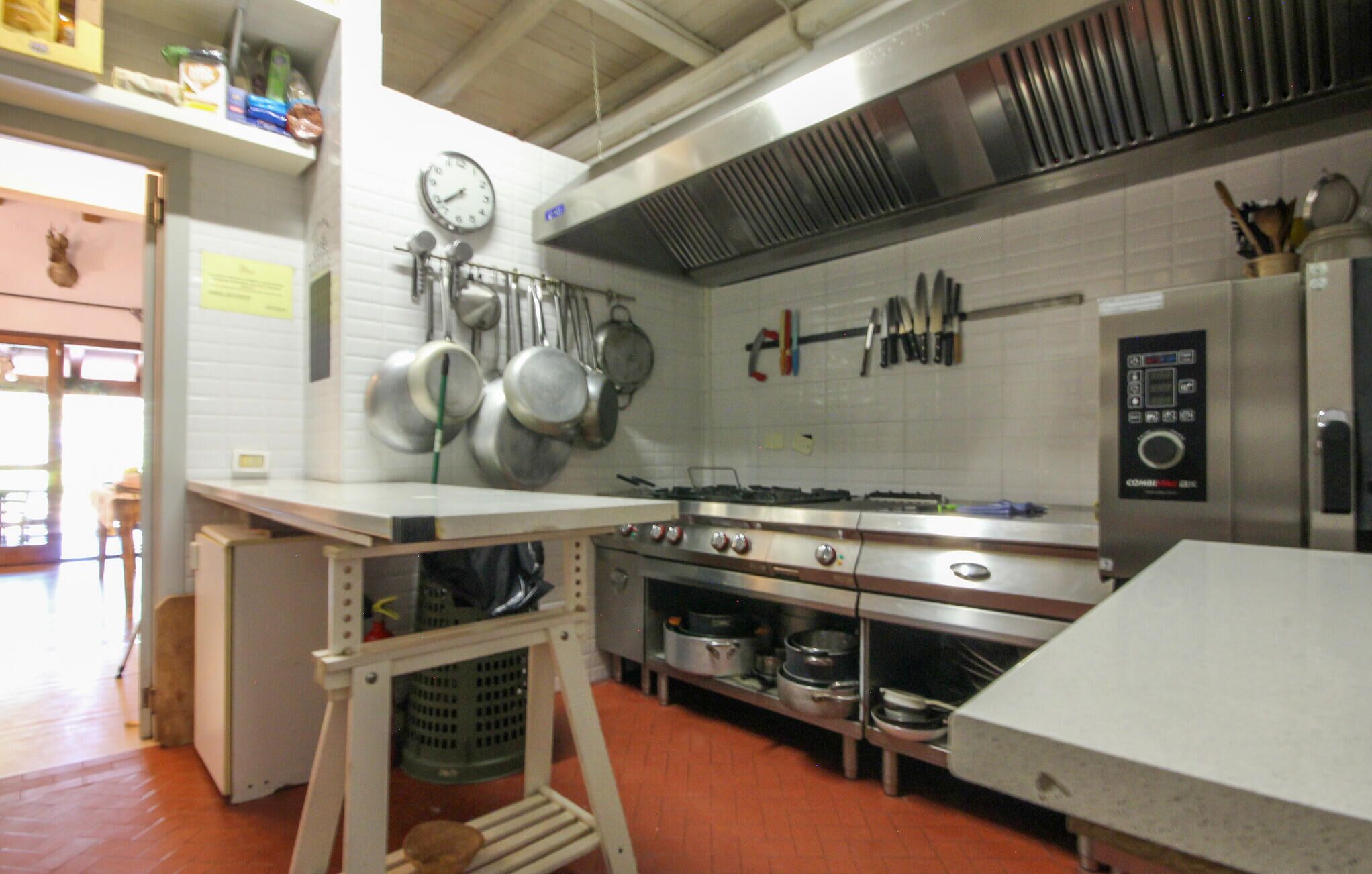 Una cocina con electrodomésticos de acero inoxidable, un reloj en la pared y diversos utensilios colgando sobre la estufa.