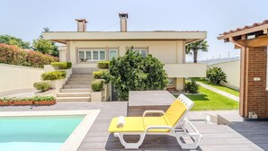 A modern house with a pool, a yellow lounge chair, and a staircase leading to the entrance.