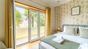 A bedroom with a bed, a nightstand, a window with curtains, and a view of palm trees.