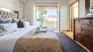 A bedroom with a large bed, a wooden dresser, and a sliding glass door leading to a balcony.