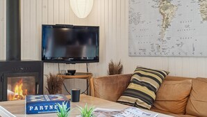 A cozy living room with a fireplace, a television mounted on the wall, a map, and a coffee table with books and magazines.