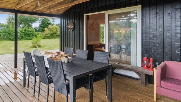 An outdoor deck with a wooden table and chairs, a dartboard, and a glass door leading to an interior space.