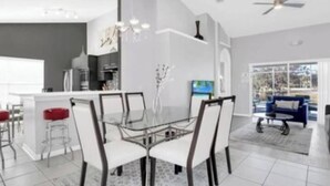 Una cocina moderna con una isla central, taburetes de bar y un comedor con mesa y sillas de vidrio.