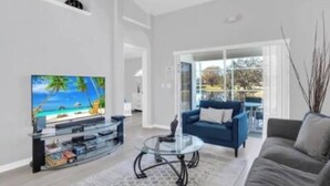 Una sala de estar moderna con un televisor de pantalla plana, un sofá azul y una mesa de centro de vidrio.