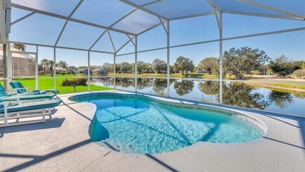 Una piscina techada con agua azul cristalina, rodeada por una estructura metálica blanca, y vista a un paisaje verde con árboles y una masa de agua al fondo.