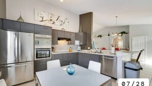 Una cocina moderna con electrodomésticos de acero inoxidable, un comedor con mesa blanca y armarios grises.