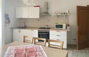 Une cuisine de taille réduite équipée d’une cuisinière à gaz, d’un four, d’un four à micro-ondes et de meubles de rangement blancs.