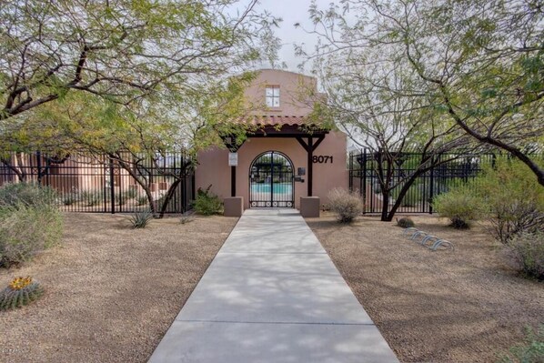 A building entrance with a number 8071 sign, a concrete pathway, and a gated area with trees. - Escape to Gold Canyon. Enjoy Mountain Views, Desert Trails&Premier Golf Courses. (Gold Canyon)