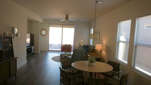 A spacious living area with a round table and chairs, a television, and a sliding glass door leading to an outdoor patio. - Escape to Gold Canyon. Enjoy Mountain Views, Desert Trails&Premier Golf Courses. (Gold Canyon)