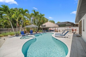A swimming pool with lounge chairs, a barbecue area, and palm trees. - New! Tiki Sunset - Luxury Heated Pool & Spa Oasis, Approx 1 Mile to Vanderbilt Beach! (Naples)