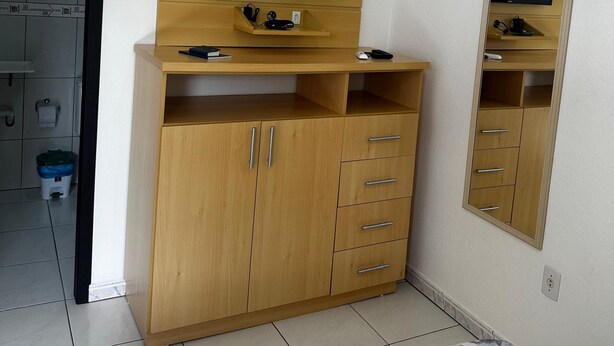 A room with a wooden cabinet, a television mounted on the wall, and a small shelf with a remote control.
