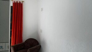 A corner of a room with a brown chair, white walls, and a red curtain.