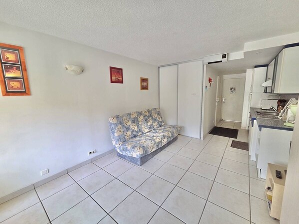 Ein Zimmer mit einer Couch, einer Küchenzeile und einer Tür zu einem weiteren Raum.