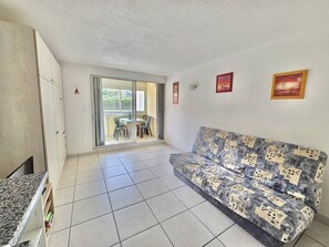 A living room with a sofa, a dining table with chairs, a sliding glass door, and a kitchen area.