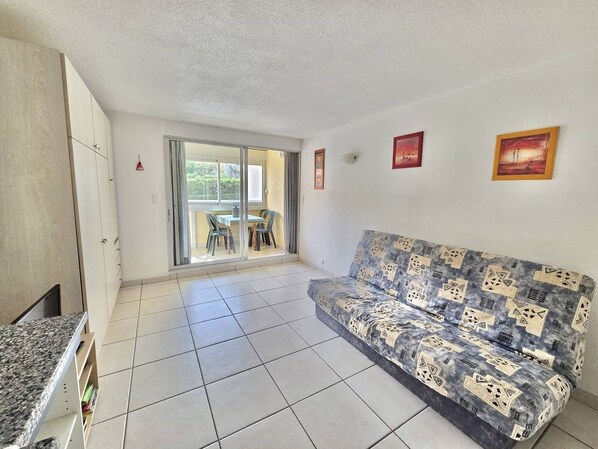 Ein Wohnzimmer mit einer Couch, einem Esstisch mit StĂŒhlen, einer SchiebetĂŒr und einer KĂŒchenzeile.
