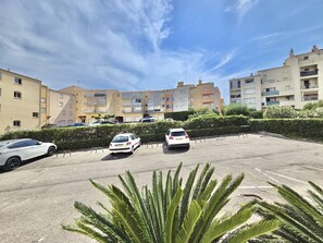 Ein Parkplatz mit zwei Autos, ein Gebäudekomplex mit Balkonen und einem klaren Himmel.