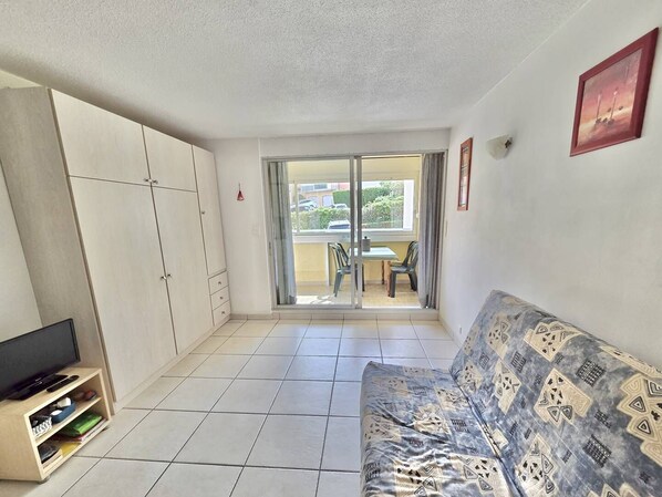 A living room with a sofa, TV stand, and a balcony with a table and chairs.
