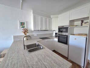 Una cocina moderna con armarios blancos, un lavamanos doble, horno empotrado y refrigerador.