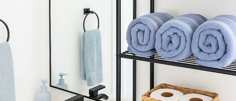 Ein modernes Badezimmer mit einem weißen Waschbecken, schwarzen Metallregalen und einem Spiegel.