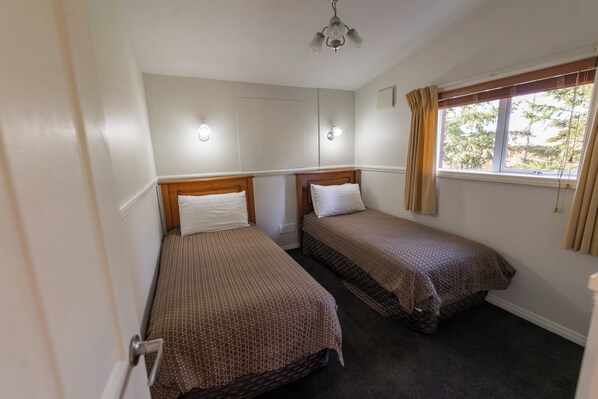 A room with two single beds, a window with curtains, and a ceiling light fixture.