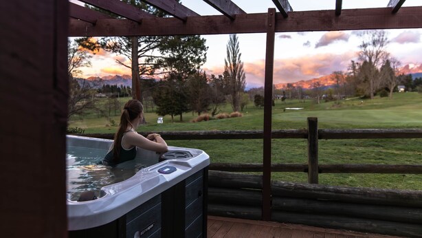 A hot tub with a view of a golf course and mountains during sunset. - Alpine Springs Motel | Hot Tub | Unit 2 - HS51212 (Hanmer Springs)