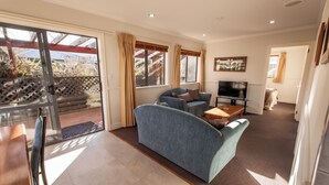 A living room with a sofa, TV, and a dining area with a table and chairs. - Alpine Springs Motel | Hot Tub | Unit 2 - HS51212 (Hanmer Springs)