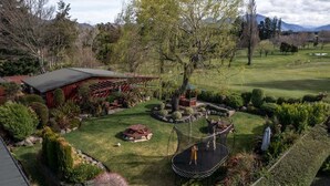 A residential property with a well-maintained lawn, a trampoline, a wooden deck, and a red barn-like structure.