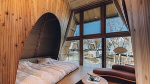 Een slaapkamer met een groot raam, een bed, een klein tafeltje en een bank.