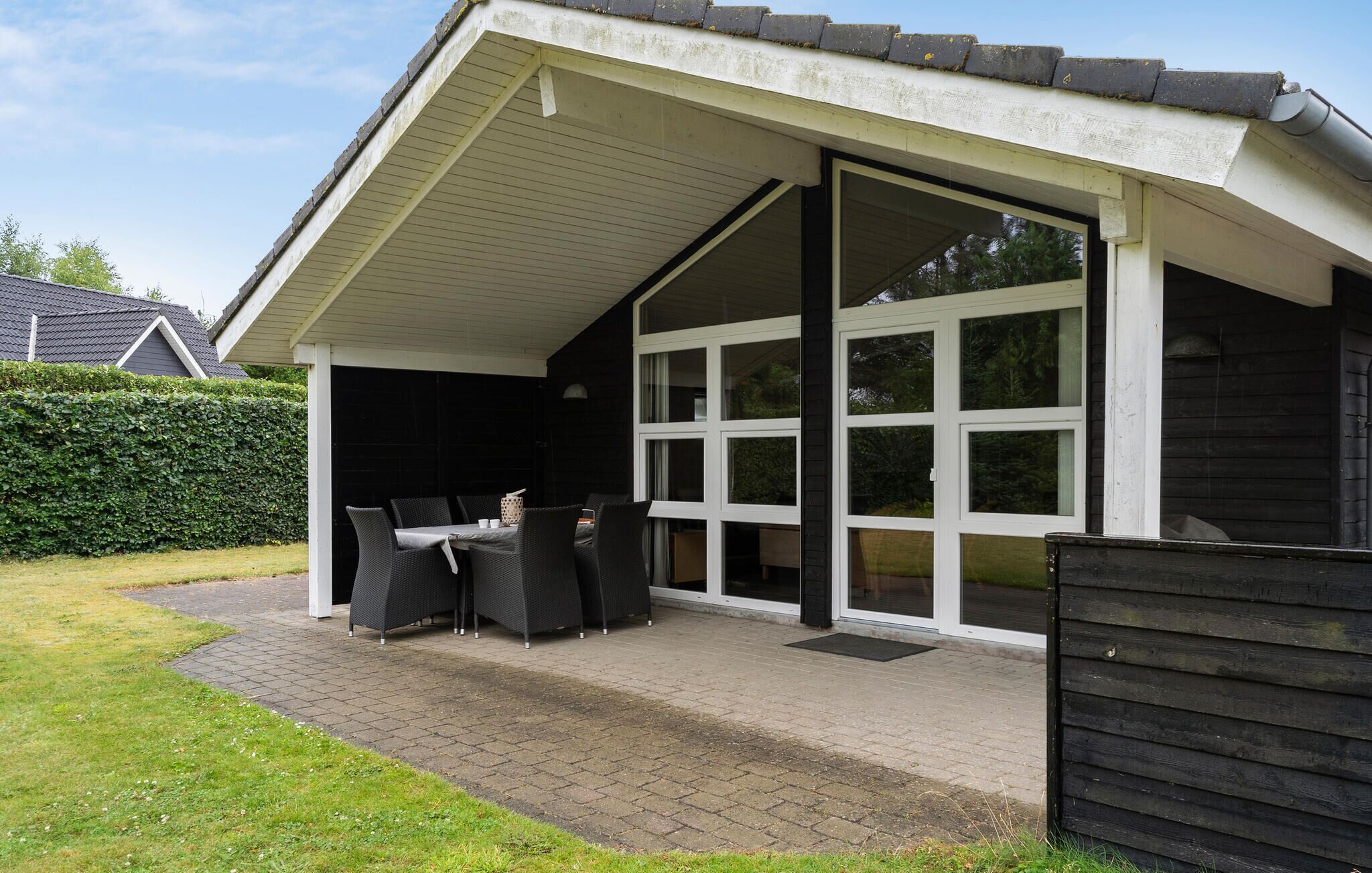 Een overdekt terras met een tafel, stoelen, een schuifpui en een houten omheining.