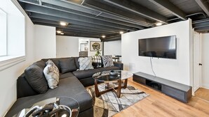 En moderne stue med en hjørnesofa, et sofabord i glas og et fladskærms-tv på væggen.