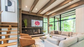 Una sala de estar moderna con chimenea, ventanas amplias y una escalera.