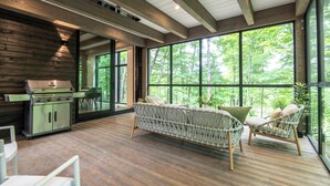 Una habitación amplia con un gran ventanal, techo de madera y zona de barbacoa.