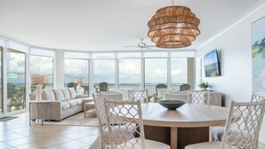A spacious room with a large dining table surrounded by wicker chairs, a sofa, and a ceiling fan.