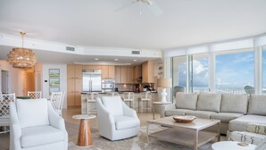 A spacious living area with a sofa, armchairs, and a coffee table. A kitchen is visible in the background with modern appliances.