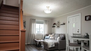A living room with a sofa, a dining table, and a staircase. - Cozy Bancroft Stay in the Minnow Lake area (Greater Sudbury)