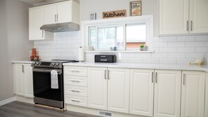 A modern kitchen with white cabinetry, a built-in oven, a toaster, and a window above the countertop. - Cozy Bancroft Stay in the Minnow Lake area (Greater Sudbury)
